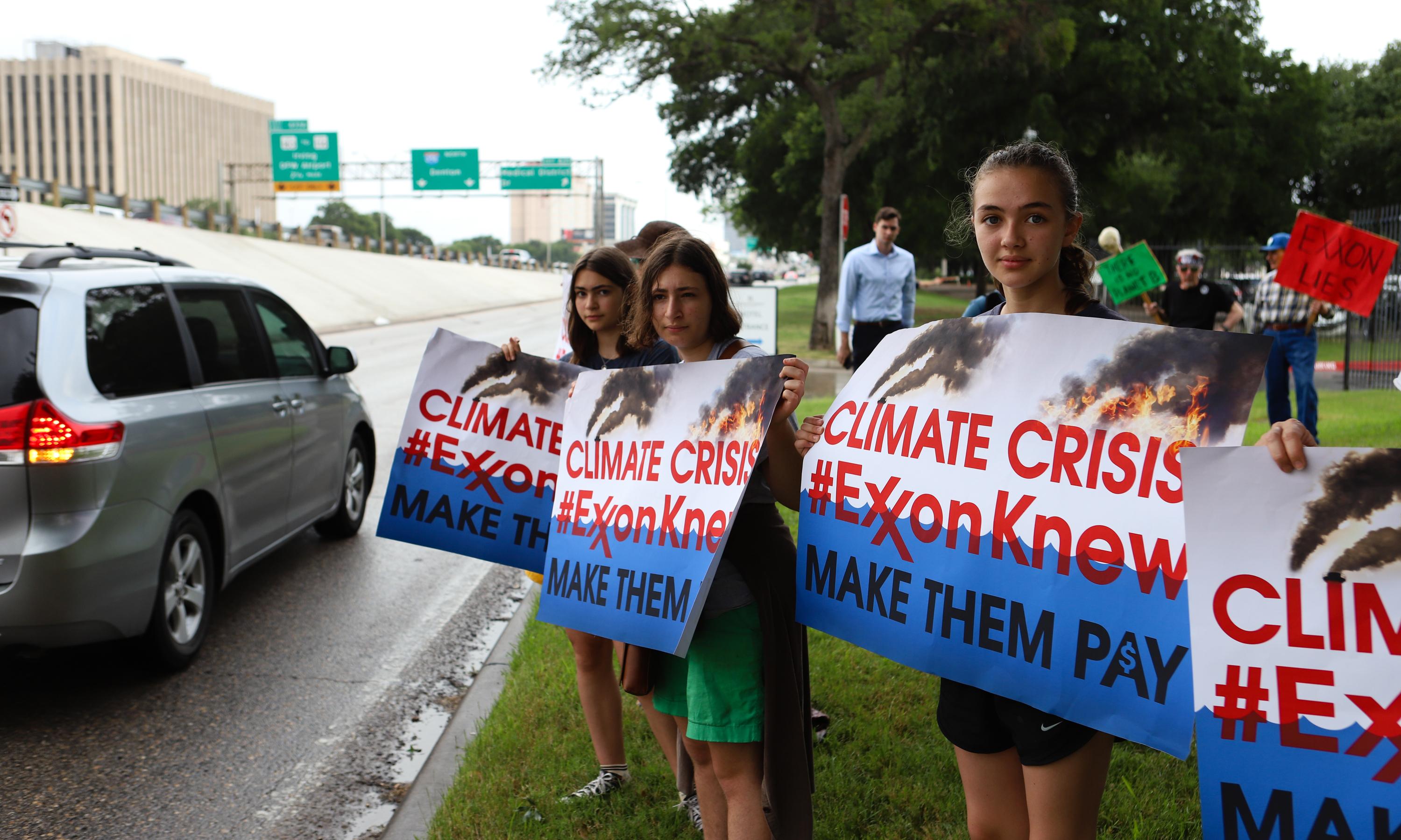 Young girls on the side of the road hold signs that read "Climate Crisis, #ExxonKnew Make Them pay."
