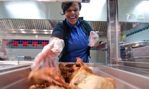 Cafeteria worker loading roast chicken onto serving trays
