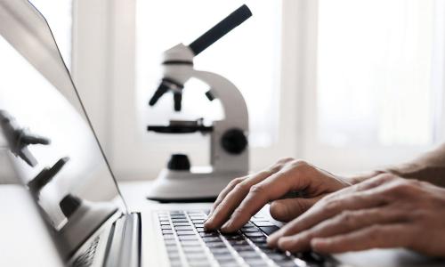 Person typing on laptop with microscope in background