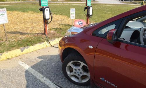 A red Nissan EV at a charging station in Maine