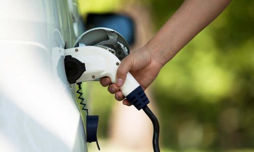 A hand plugs in a charger into a white electric vehicle