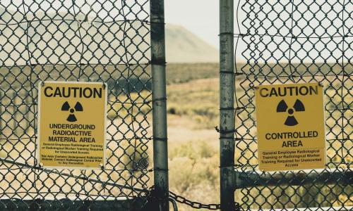 Fence with radiation warning signs and desert landscape in background