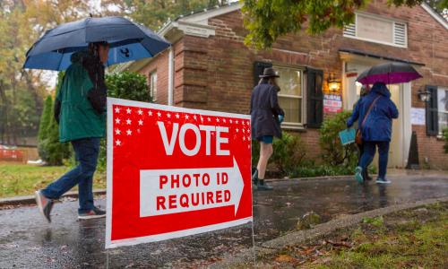 Voters walking to polling place in the rain, with sign saying photo ID required